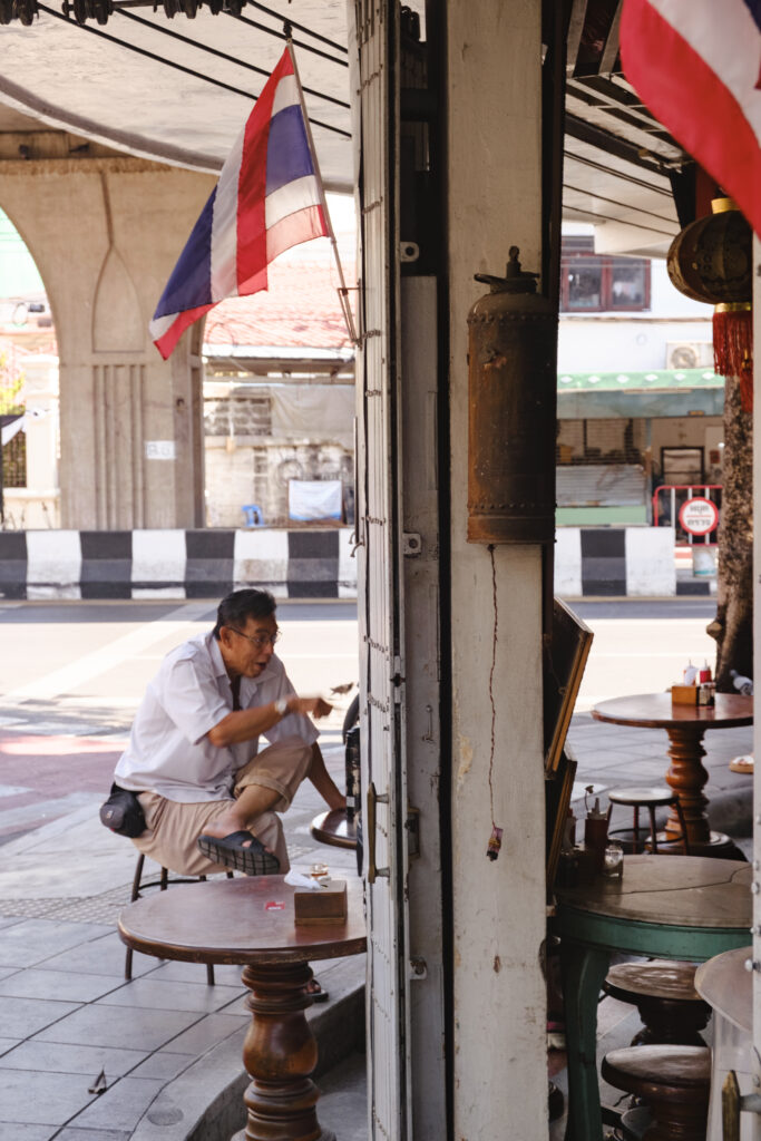 Hombre sentado en cafetería antigua en Bangkok sonriente en la calle